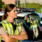 Police officer in a high-visibility vest with a camera on a car, surrounded by police vehicles.
